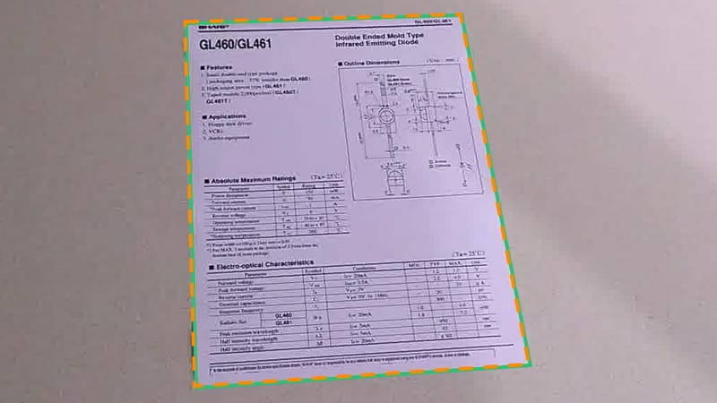 A page on a grey round table with the true outline in green and the model's suggested corners in dashed orange, almost on top of it.